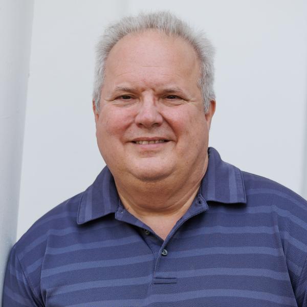 A headshot of lance hill in a blue collared shirt in front of the feldman building. 