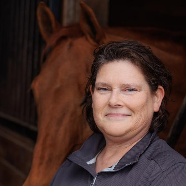 A headshot of Rebecca Splan at the equestrian center in front of a horse. 