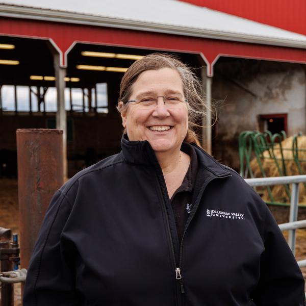 A headshot of Joanne Powell in a black delval zip up jacket in front of the dairy barn. 