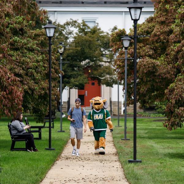 Caesar the mascot is walking with a student on the quad. 