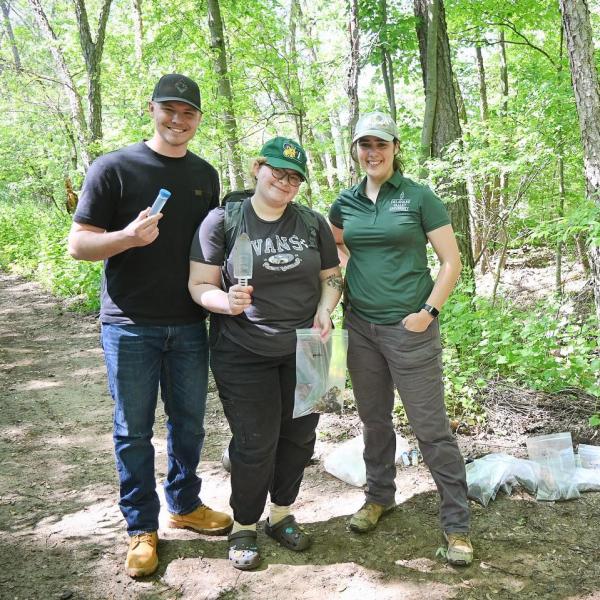 Students and professor fiola are in a wooded area posing for a picture. 