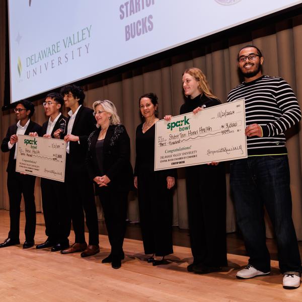 The winning spark bowl team is on stage with big checks. 