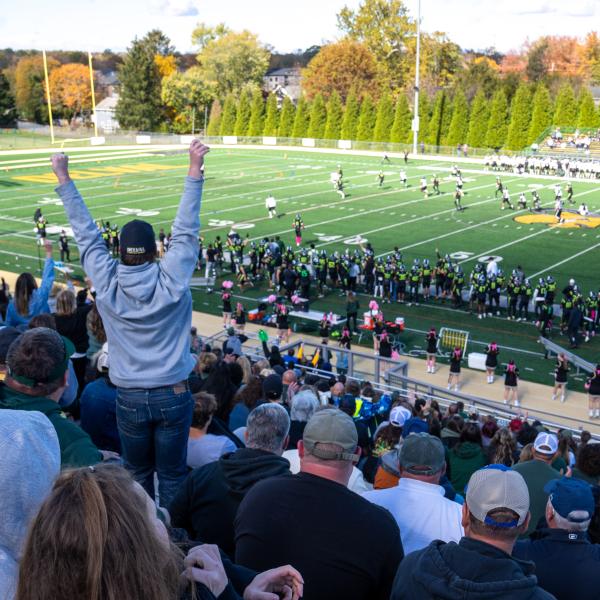 An audience member is cheering on the football team from the stadium seats. 