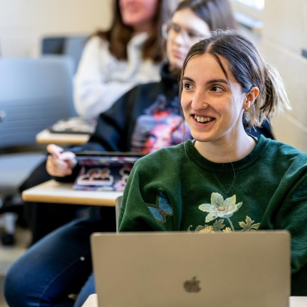 A female student is sitting at her desk in class smiling at the professor. 