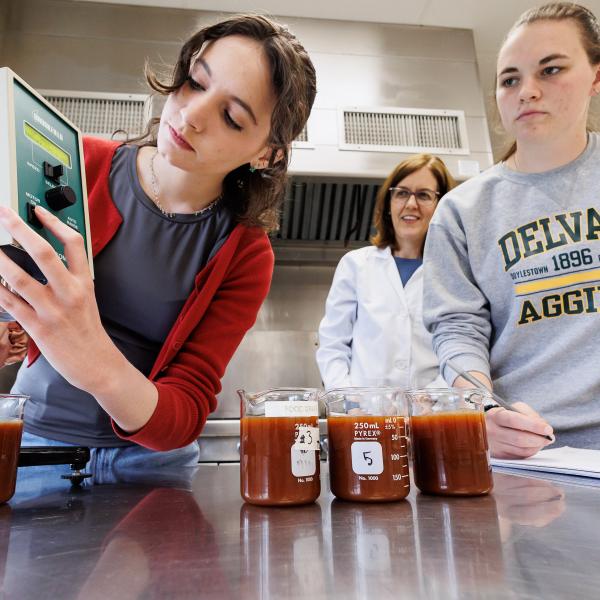 A female student is working with another student in the food science lab to fill beakers of liquid.