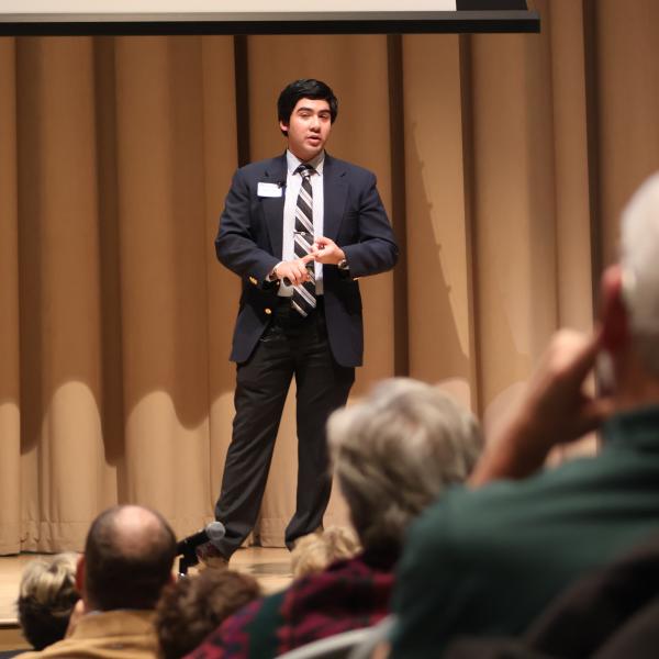 A male business student is on stage in the auditorium wearing formal business attire.