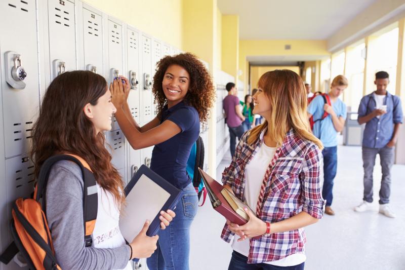 High school students talk while holding books by a row of lockers. 