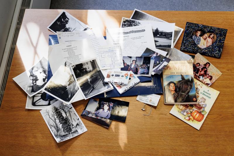 A folder with photos, cassette tapes, and papers are protruding out of an open folder on a desk. 