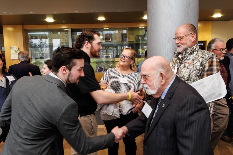 Student Tony Rago '22 is dressed in suit and tie and shaking hands with Jim Diamond. 