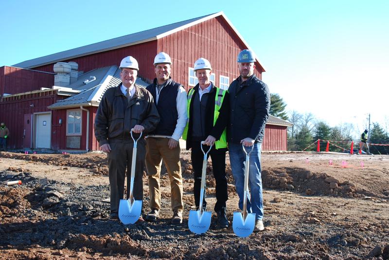 Dr.Benjamin Rusiloski and several Blue Rock workers are lined up for a photo wearing helmets and holding shovels on the grounds where terrain will be built
