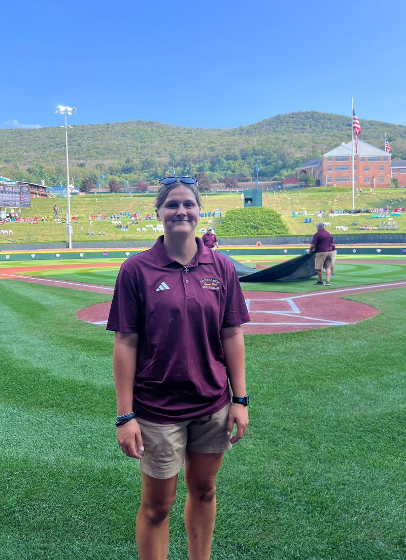 Jillian is standing on a turf field smiling at the camera. 