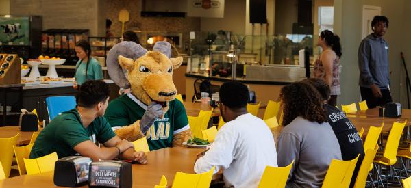 Caesar is in the dining hall sitting with students in the cafe area. 