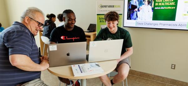 Two students are working with Lance Hill a business administration professor at a table with a laptop.