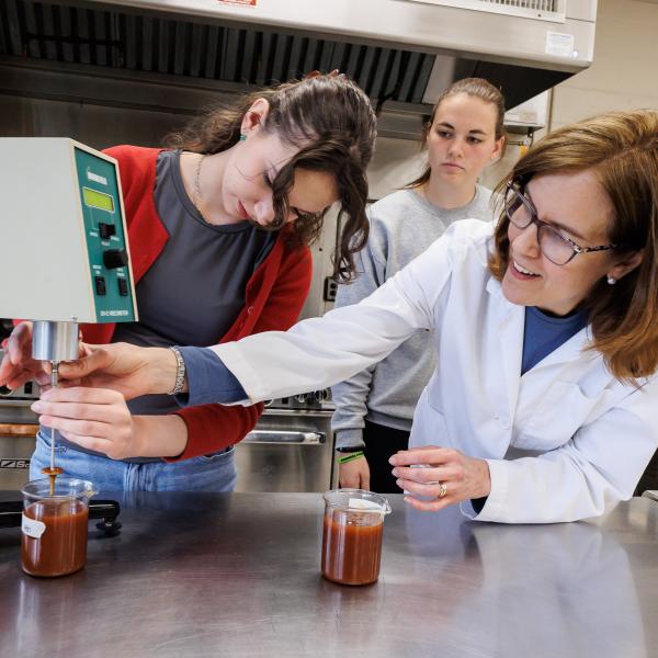 two students and a professor are using food science technology with beakers in the food science lab