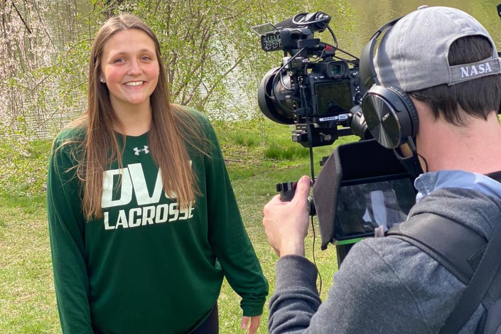 A student is being filmed with video camera, microphone and lighting, in front of Lake Archer. 